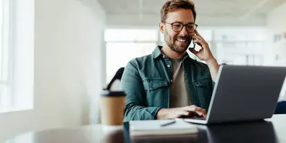 Travel manager on the phone at his laptop in the office, negotiating hotel rates for his company’s MICE procurement