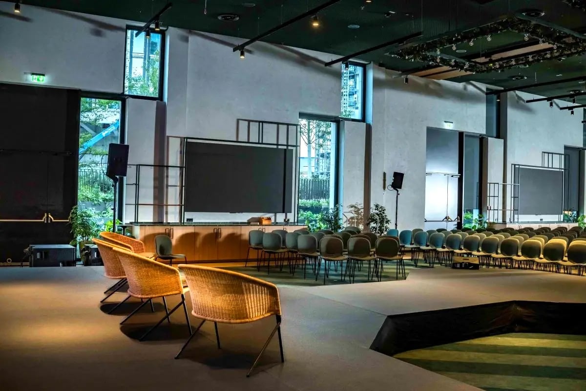 Großer Veranstaltungsraum im Scandic Hotel Frankfurt Hafenpark mit Bühne, mehreren Sitzreihen und drei geflochtenen Sesseln im Vordergrund.