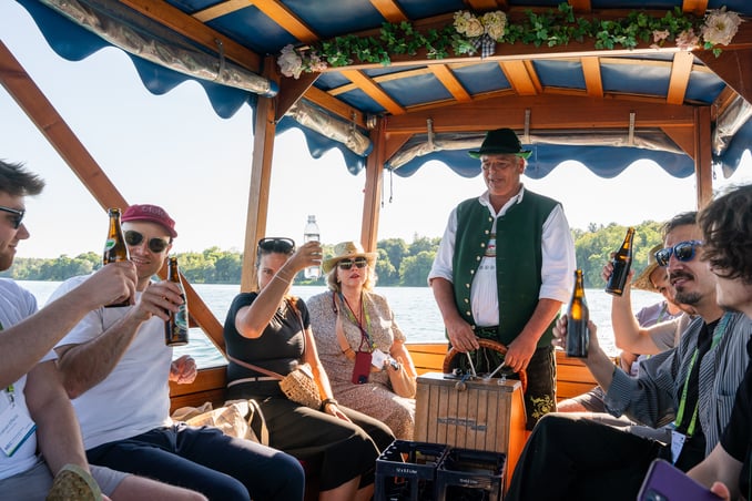 Boat captain in traditional Bavarian attire during a ferry crossing on Lake Starnberg at the MICE Executive Circle 2026 (MEC 2026). As part of the evening social program, participants of the MICE Portal industry event enjoyed time on the water, engaging in relaxed conversations beyond the official agenda. The ferry ride on Lake Starnberg was one of the networking highlights of the MEC.