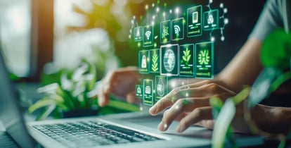 Hand tippt auf Laptop-Tastatur vor digital schwebenden Icons zu Nachhaltigkeit und Technologie