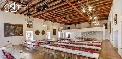 Großer, heller Seminarraum mit Holzbalkendecke, langen Tischen und Stühlen, vorbereitet für eine Veranstaltung