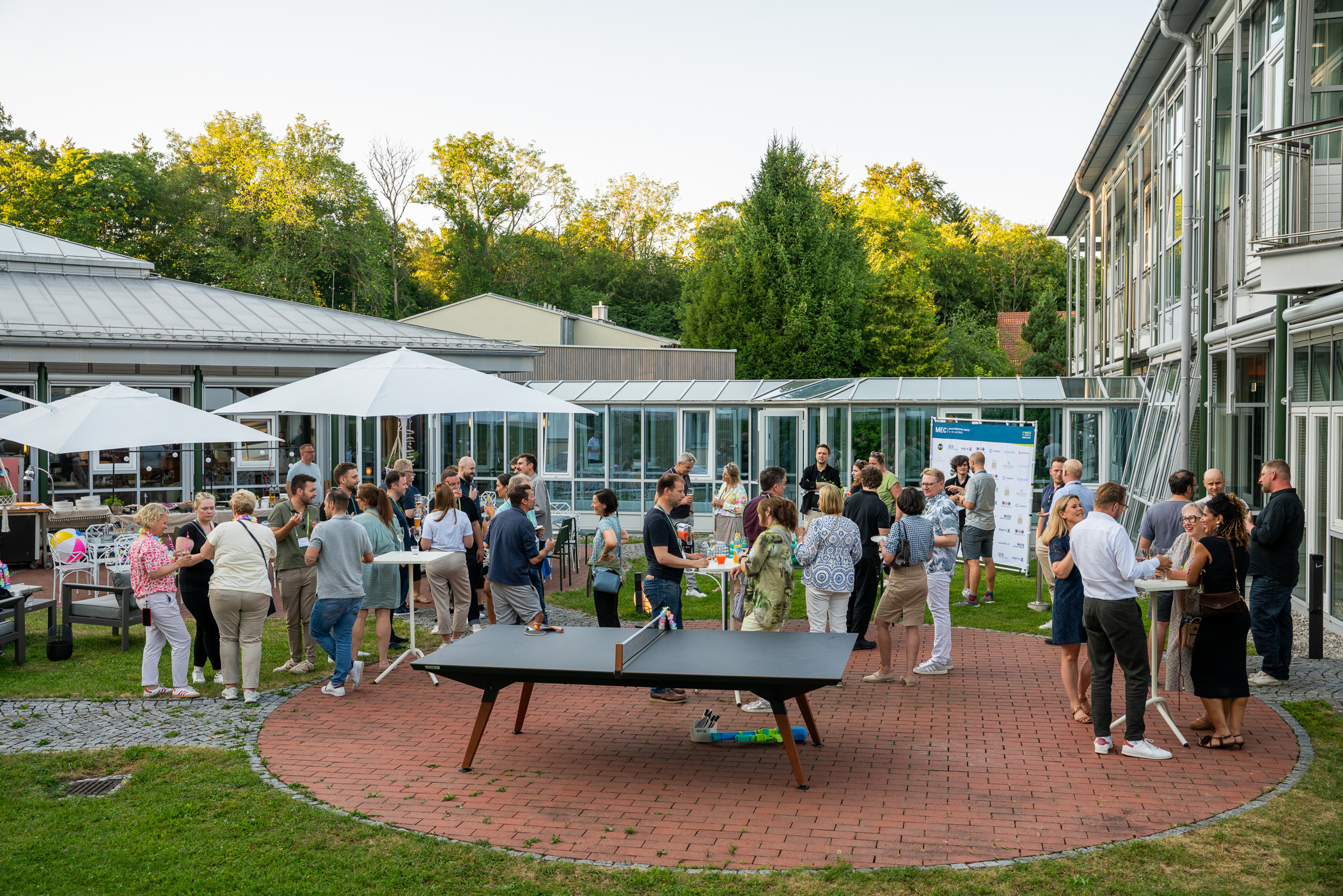 Participants in the MICE Executive Circle 2026 (MEC 2026) networking outdoors at Chateauform on Lake Starnberg in Feldafing, the first Chateauform seminar center in southern Germany. Event managers, buyers, and suppliers from the MICE industry gather in small groups to exchange ideas outdoors, with the conference venue’s gardens visible in the background. MEC 2026 is MICE Portal’s annual industry gathering focused on strategic MICE management and digital event procurement.
