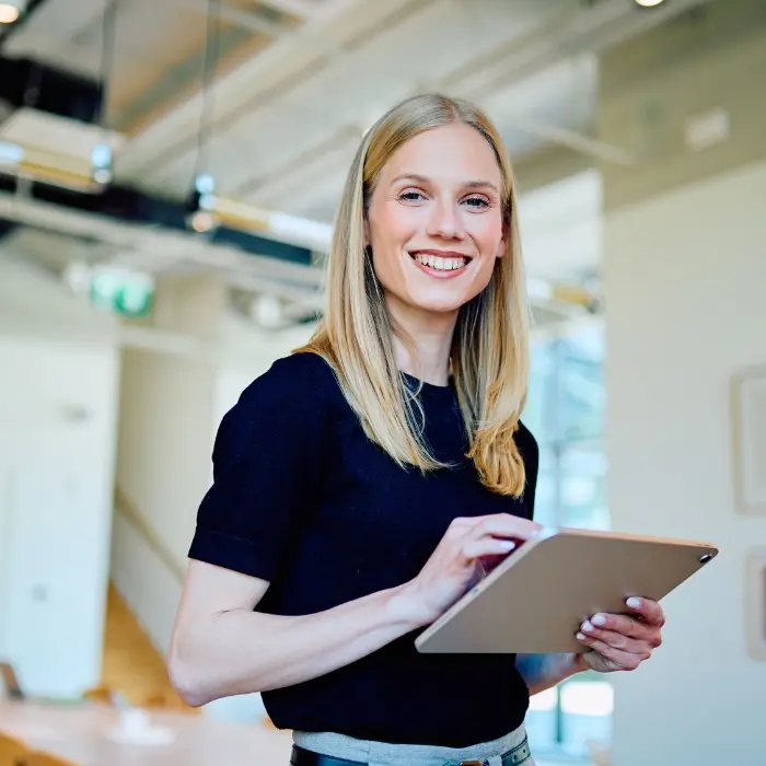Lächelnde Frau mit Tablet in einem modernen, hellen Büro, selbstbewusst und zielgerichtet, symbolisch für die Phase Gestalten im Strategischen MICE Management.