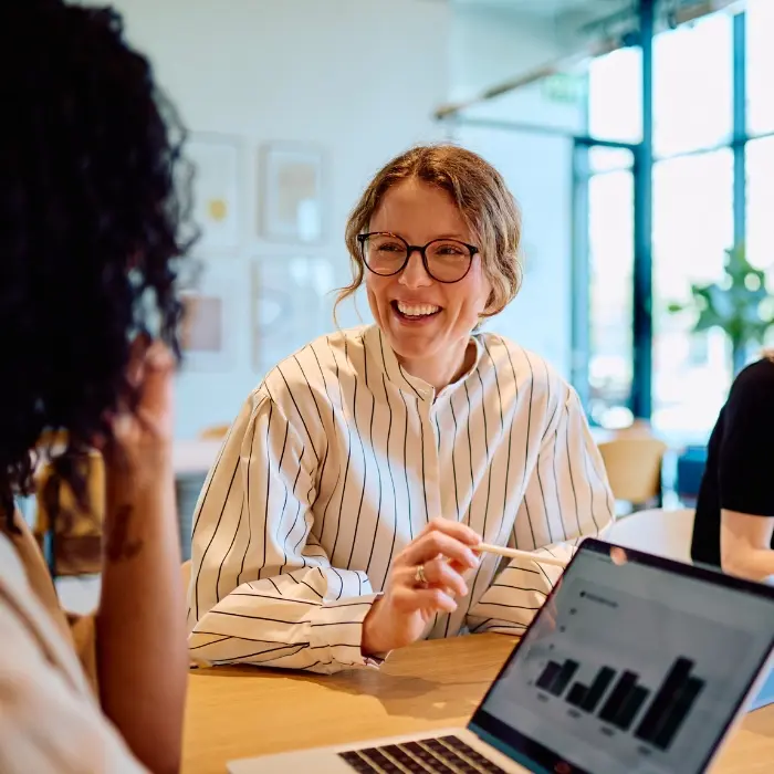 Lächelnde Frau mit Brille bespricht Kennzahlen auf einem Laptop, symbolisch für die Analyse-Phase Orientieren im Strategischen MICE Management